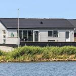 Ein Haus mit Terrasse direkt am Wasser. Fenster und Türen sind sichtbar.