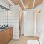 Badezimmer mit Waschbecken, Spiegel, Dusche und Toilette. Holzdecke und Fliesen.