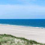 Weiterer Blick auf den Strand mit Sanddünen und dem offenen Meer.