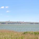 Weitläufiger Blick auf Wasser und Küstenstadt mit Leuchtturm im Hintergrund.