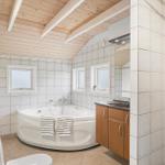 Badezimmer mit Badewanne, Waschbecken und Toilette. Holzdecke und Fliesenwände.