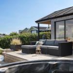 Terrasse mit Sitzgruppe und Whirlpool. Modernes Haus mit Glasfront und Holzverkleidung.
