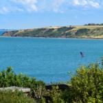 Meer mit Windsurfer und grüner Küstenlandschaft im Hintergrund.