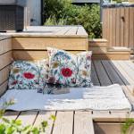 Terrasse mit Holzbank, Kissen und Decke für entspannte Sonnenstunden.