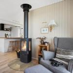 Wohnzimmer mit Kamin, grauer Sessel und Küchenbereich im Hintergrund.