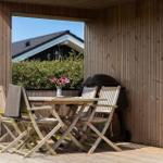 Terrasse mit Holztisch, vier Stühlen und Grill. Blick auf grüne Hecke und Haus.