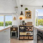 Küche mit hellen Wänden, Holzoberflächen und Blick auf grüne Außenbereiche.