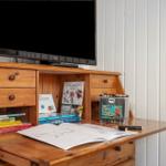 Holzschreibtisch mit Fernseher, Büchern und Malutensilien.