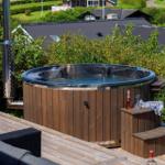 Ein Whirlpool auf einer Terrasse mit Blick auf grüne Bäume und Häuser.