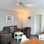 Wohnzimmer mit Sofa, Sesseln und Fernseher. Holztisch und Stehlampe sichtbar.