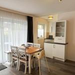 Essbereich mit Tisch und Stühlen, Küchenzeile und Fenster mit Vorhängen.