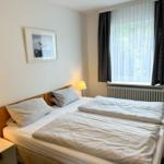 Schlafzimmer mit Doppelbett, Nachttisch und Fenster mit Vorhängen.