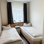 Zwei Einzelbetten mit weißen Bettwäsche stehen unter einem Fenster mit Vorhängen.