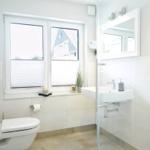 Badezimmer mit Toilette, Waschbecken und Dusche. Fenster mit Jalousie und Pflanze.