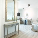 Eingangsbereich mit Spiegel und Konsole. Im Hintergrund Wohn- und Essbereich mit Sofa und Tisch.