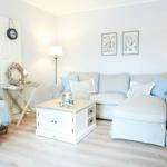 Wohnzimmer mit Sofa, Kaffeetisch und Sessel. Wandbilder und Stehlampe sind sichtbar.