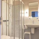 Bad mit Dusche, Waschbecken und Toilette. Weiße Fliesen und Spiegel.