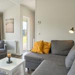 Wohnzimmer mit Sofa, Sessel und Tisch. Anblick auf Terrasse und Garten.