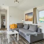 Wohnzimmer mit grauem Sofa, Tisch und Fenster mit Blick auf Grünflächen.