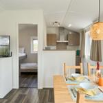 Küche, Essbereich und Schlafzimmer in einem Ferienhaus. Tisch gedeckt, TV eingeschaltet.