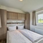 Zwei Einzelbetten mit weißen Bettwäsche, Holzmöbel und Fenster mit Blick auf Grünfläche.