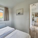 Schlafzimmer mit Bett, Fenster und Blick in die Küche.