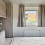Schlafzimmer mit Bett, Schrank und Fenster mit Blick auf Außenbereich.