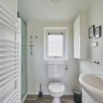 Badezimmer mit Dusche, Toilette und Waschbecken. Fenster und Spiegel sichtbar.