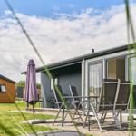 Terrasse mit Tisch, Stühlen und Sonnenschirm vor grauem Ferienhaus.