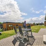 Terrasse mit Tisch, Stühlen und Grill. Hintergrund: moderne Holzhäuser und Grünfläche.