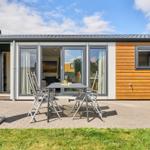 Terrasse mit Tisch, Stühlen, Sonnenschirm und Grill. Durchgehende Glastüren zum Innenraum.