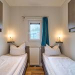 Zwei Einzelbetten mit weißen Bettwäsche, Fenster mit blauer Vorhang und Nachttische mit Lampen.