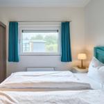 Schlafzimmer mit Bett, Nachttisch und Fenster mit Vorhängen.