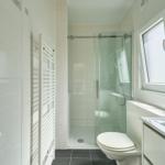 Badezimmer mit Dusche, Toilette und Waschbecken. Fenster und Heizung sind vorhanden.