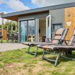 Zwei Liegestühle stehen auf dem Gras vor einem Chalet mit Terrasse und Grill.