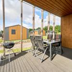 Terrasse mit Grill, Tisch und Stühlen. Hintergrund: Grasfläche und Holzhaus.
