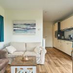 Wohnbereich mit Sofa, Couchtisch und Küche im Hintergrund.