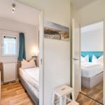 Zwei Schlafzimmer mit Betten, Fenster und Holzboden. Wandbild zeigt Strand.