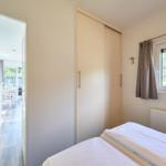 Zwei Betten, Schiebetürenschrank und Fenster mit Blick auf Wald.