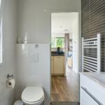 Badezimmer mit Toilette, Waschbecken und Heizkörper. Durchgang zu Küche und Wohnbereich.