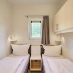 Zwei Einzelbetten mit weißen Bettwäschen, kleiner Nachttisch und Fenster mit Vorhang.