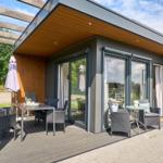 Terrasse mit Sitzgruppe und Tisch unter Holzüberdachung. Glasfront öffnet sich zum Innenraum.