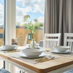 Esstisch mit Stühlen und Platz für vier Personen vor großen Fenstern.