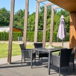 Terrasse mit Tisch und Stühlen unter Pavillon. Hintergrund: Gras, Bäume und Hecke.