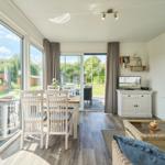Wohn- und Essbereich mit großem Fenster und Terrasse. Möbel aus Holz und Rattan.