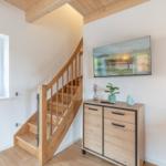 Holztreppe führt zur oberen Etage. Wandbild, Schrank und Fenster sichtbar.