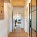 Flur mit Holzboden und Deckenbalken. Türen führen in Wohn- und Essbereich.