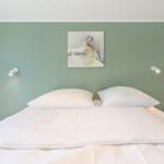 Doppelbett mit weißen Laken, grüne Wand und Wandbild mit Vogel.