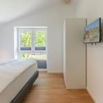 Schlafzimmer mit Bett, Fenster und Wand-TV.