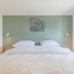 Doppelbett mit weißer Bettwäsche, grüner Wand und Wandbild mit Schmetterlingsraupe.